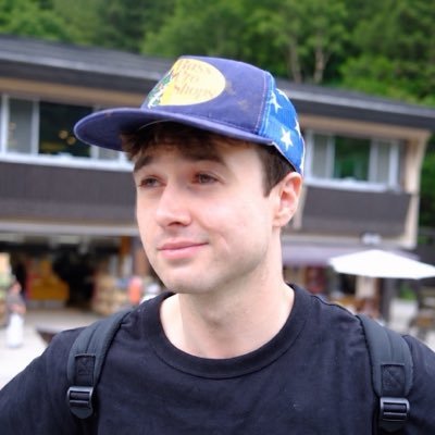Retrato de Jacob Coxon usando boné azul ao ar livre, em seu perfil público no X.