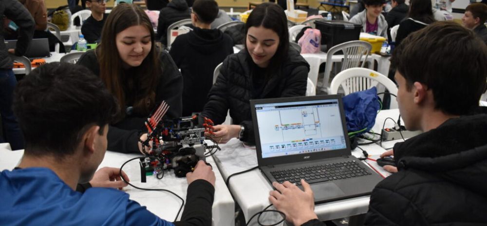 Estudantes trabalham com um robô e um notebook em uma mesa.